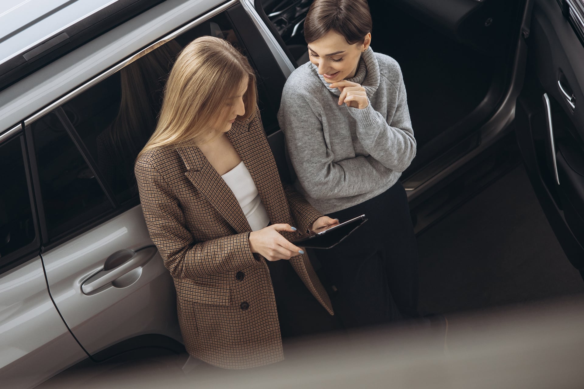 two ladies viewing an ipad next to a car
